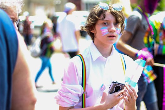 Young person with face paint and a flag participates in a vibrant LGBTQ pride parade.