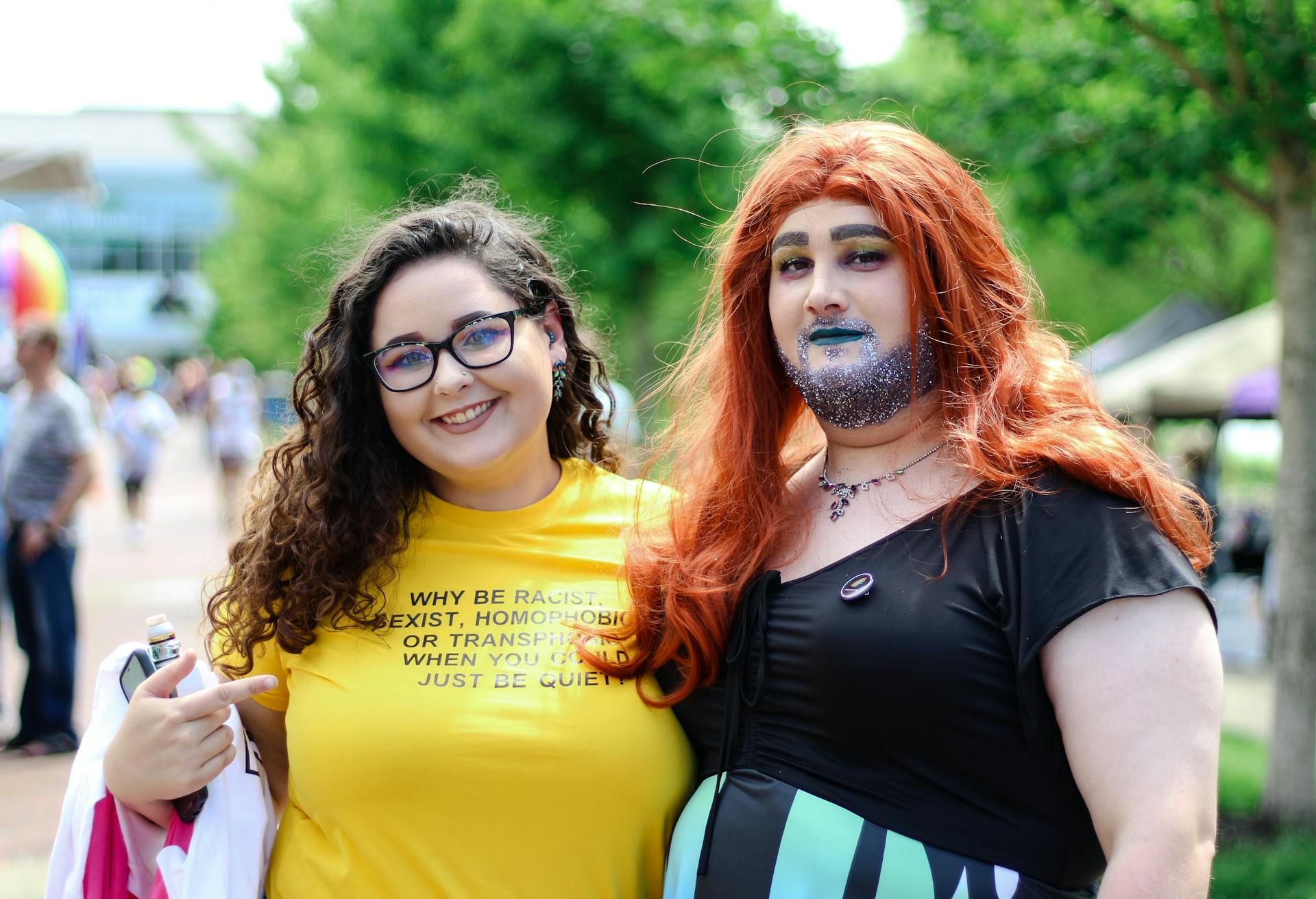 Two individuals celebrating LGBTQ Pride in vibrant outfits, outdoors at a festival.