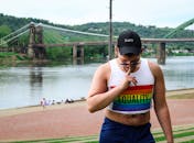 在风景优美的河桥附近，一位穿着彩虹平等上衣和帽子的男子显得格外自信