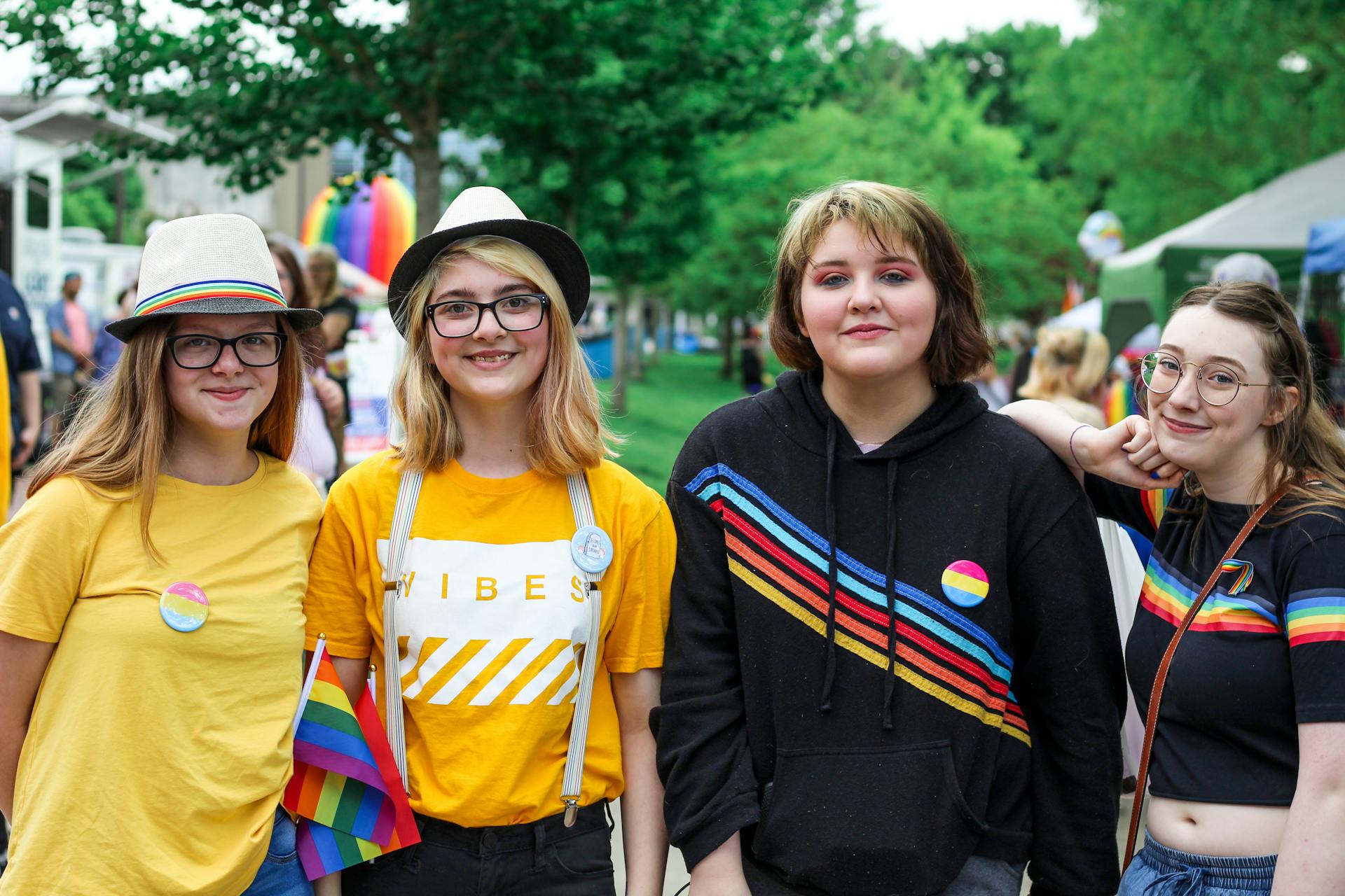 Friends enjoying a vibrant pride parade with rainbow flags and colorful outfits outdoors.