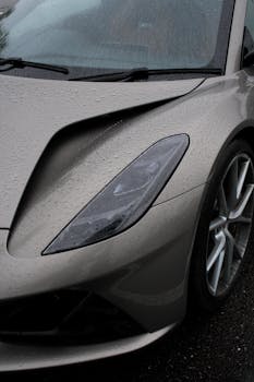 Close-up of a sports car headlight during a rainy day, highlighting design and details.