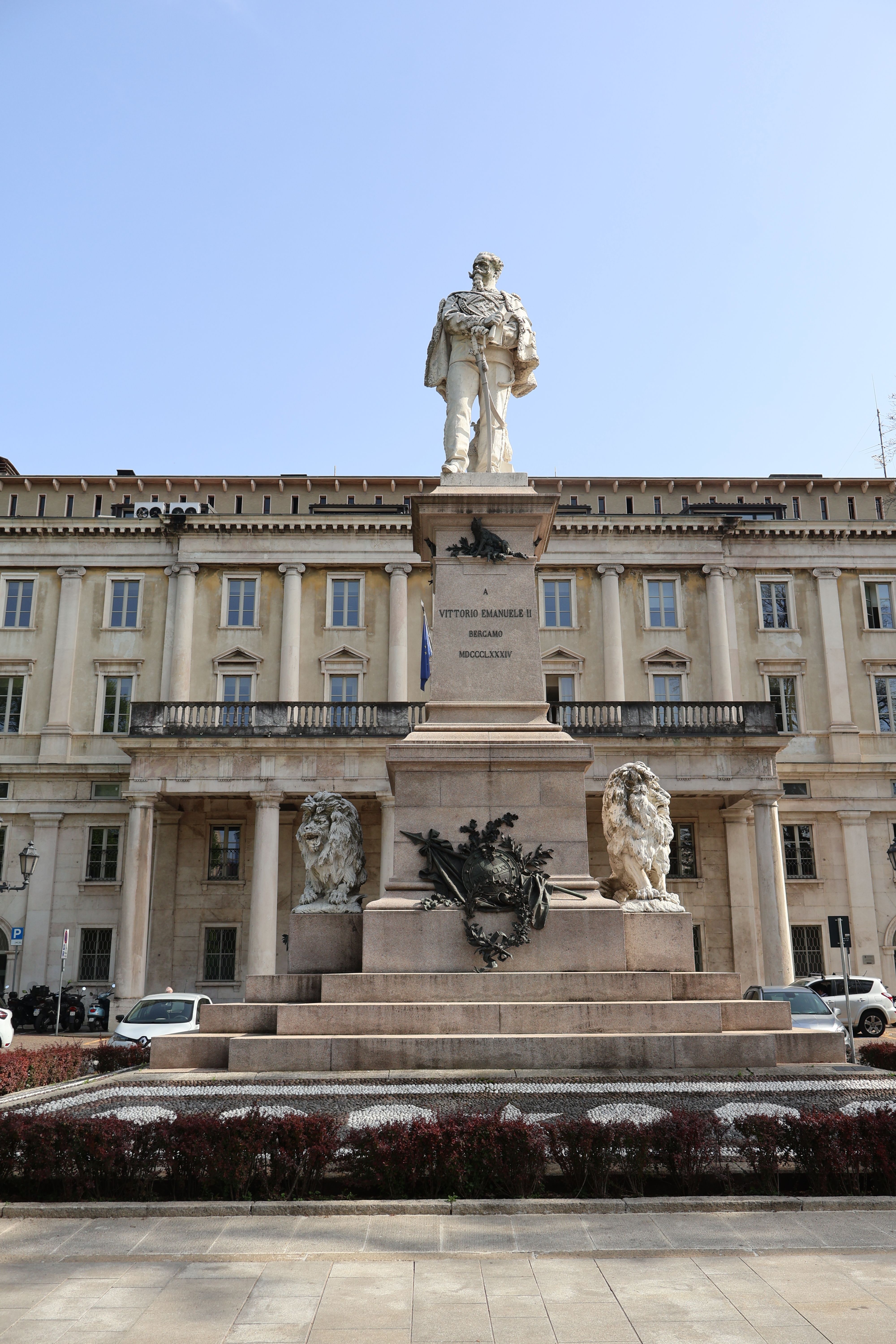 Statue of Vittorio Emanuele II in front of a historic building under a clear blue sky in Bergamo, Italy.