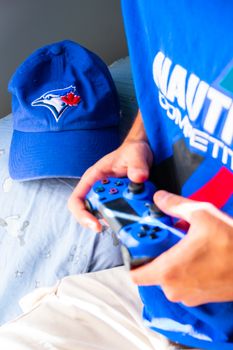 Close-up of a person holding a game controller wearing a blue baseball cap and shirt.