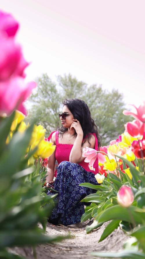 A woman in pink sunglasses sitting in a field of tulips