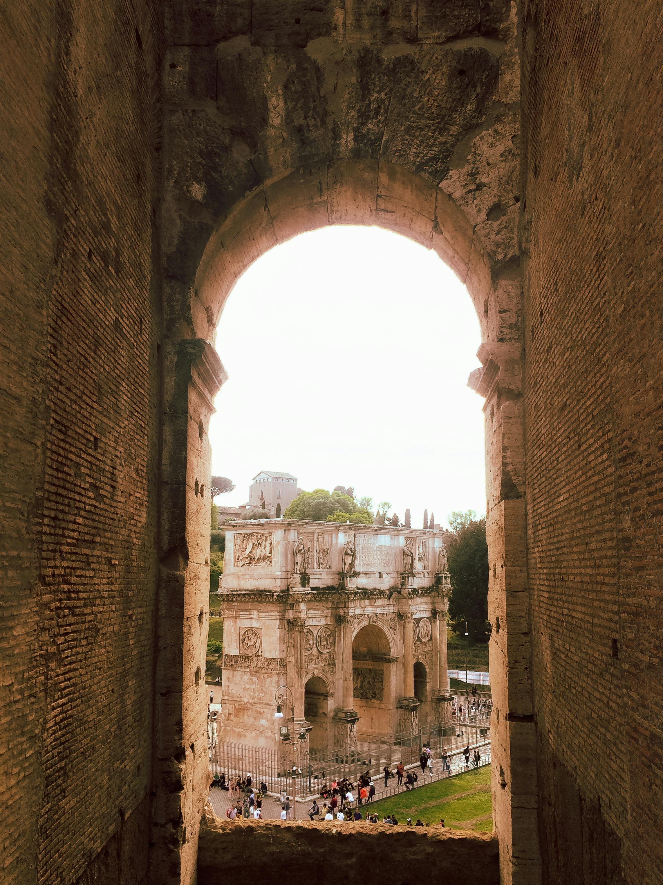 Historic view of Rome's Arch of Constantine through an ancient archway, capturing architectural grandeur.