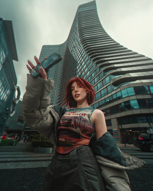 A woman with red hair is standing in front of tall buildings