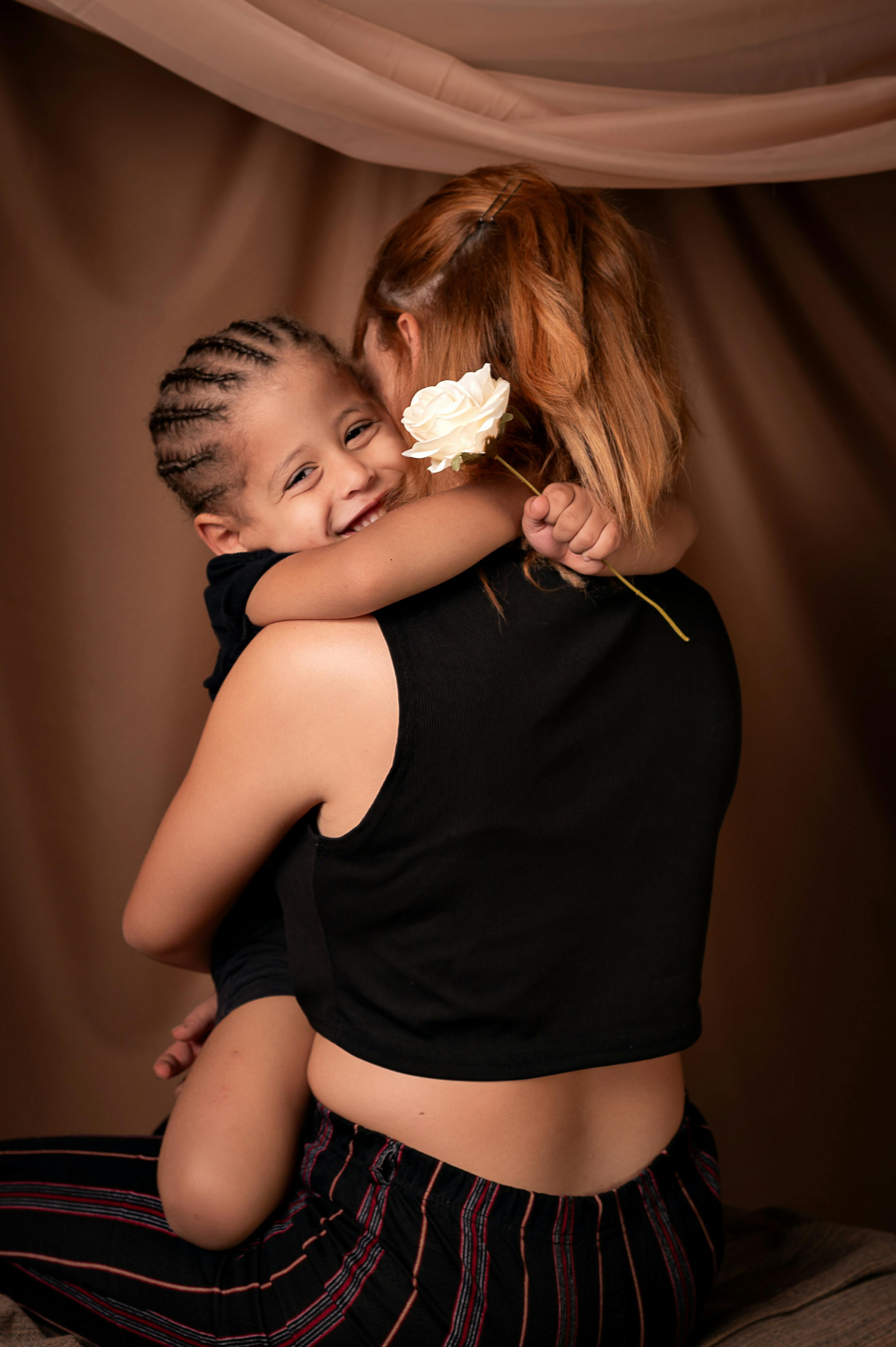A mother and daughter sharing a joyful hug holding a white rose.