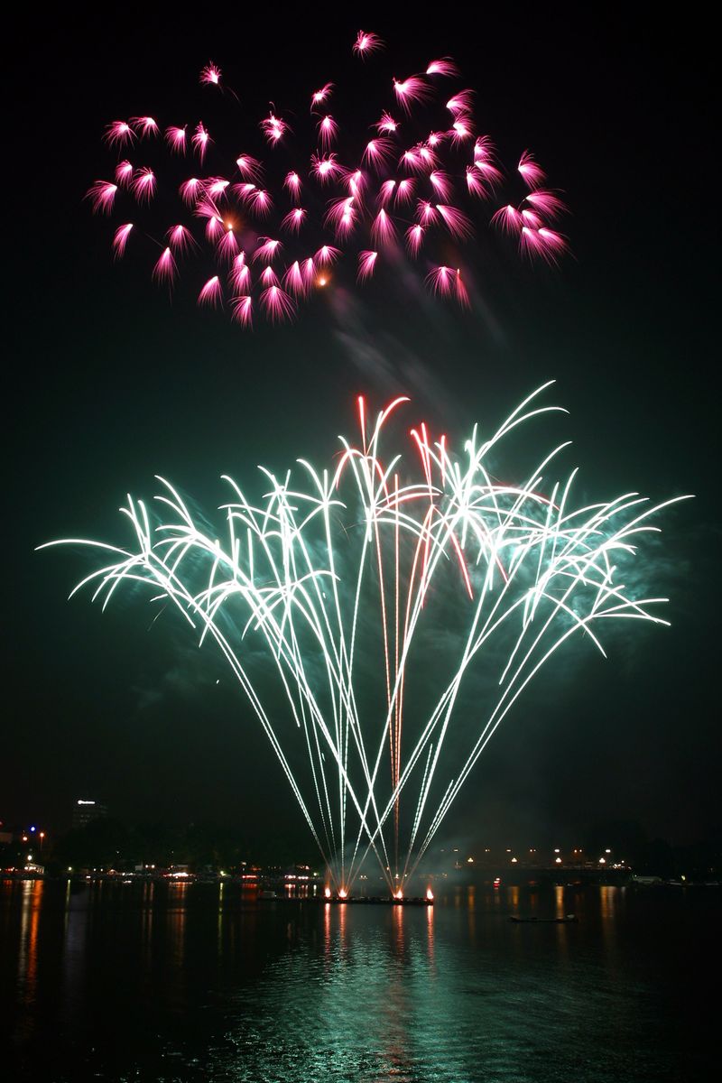Fireworks bursting over harbour waters at night with colourful reflections