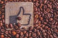 一堆烤咖啡豆上放着一个木制竖起大拇指的符号，代表欣赏