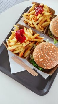 Top view of juicy burgers and crispy fries with ketchup served on a tray.