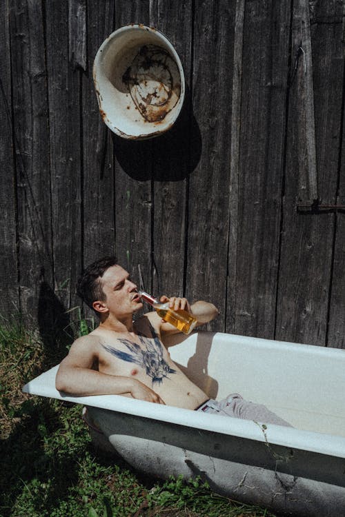 young guy relaxing with a beer in the countryside in an empty bathtub