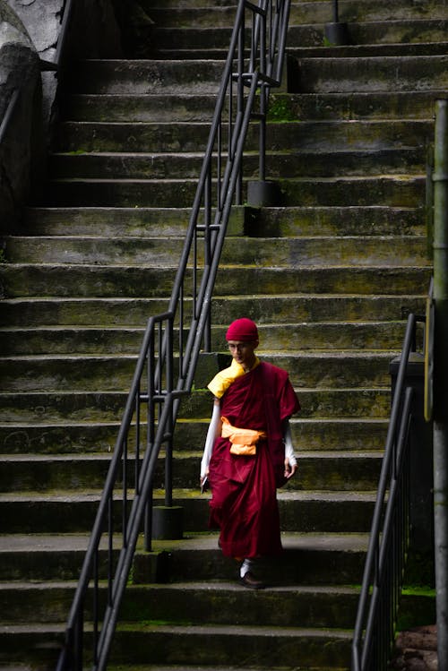 A monk walking down some stairs in a red robe