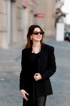 Stylish woman in sunglasses and black suit posing on a city street, exuding confidence and elegance.