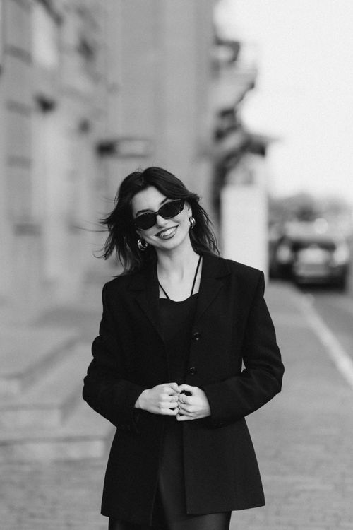 Free Stylish woman in black jacket and sunglasses smiling in urban setting. Stock Photo
