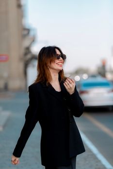 Stylish woman in sunglasses and black suit jacket posing on city street.