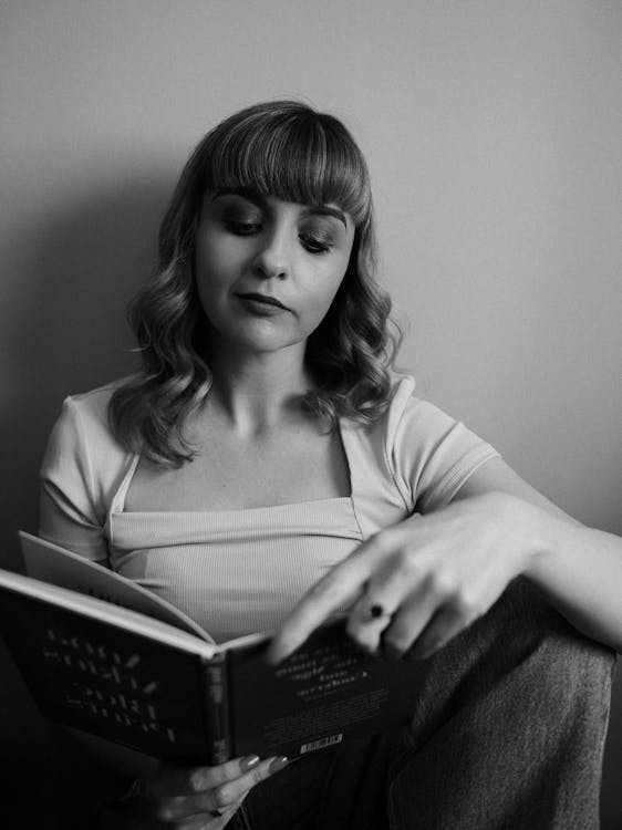 Black and White Photo of a Young Woman Sitting and Reading a Book 