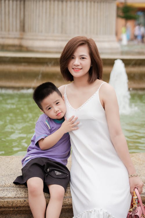 A woman and a boy pose for a photo in front of a fountain
