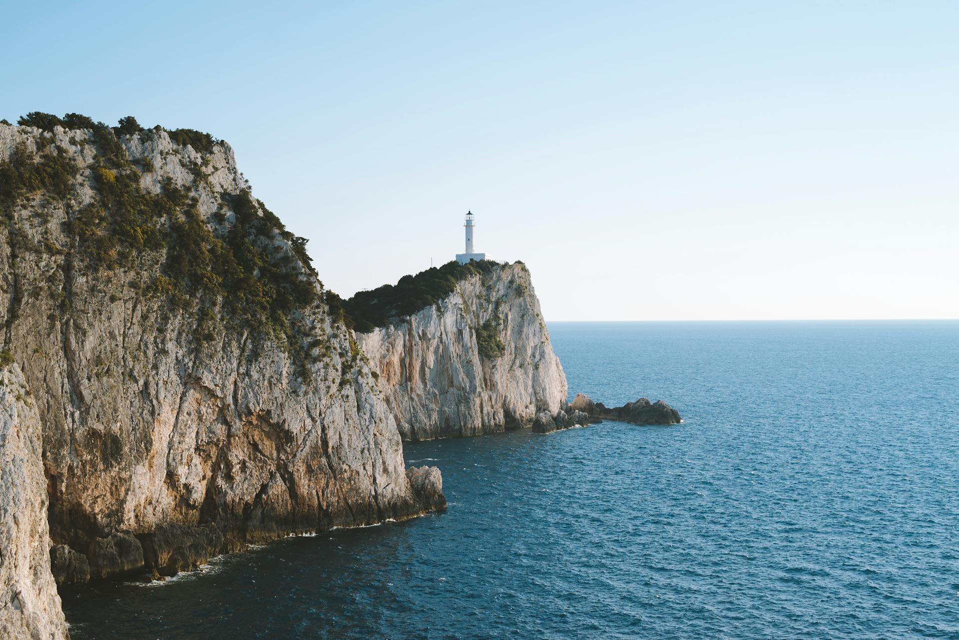 A scenic view of a lighthouse perched on a cliff in Thera, Greece, overlooking the azure sea.