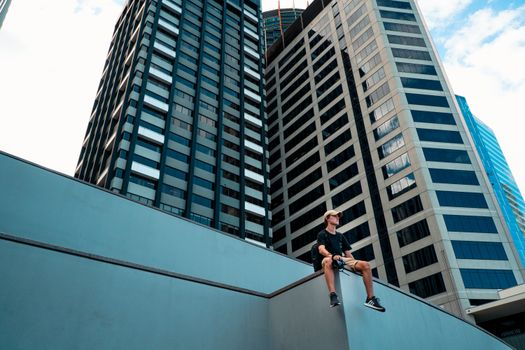 男人坐在壁架上，背景是现代摩天大楼林立的城市景观