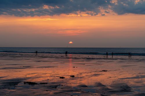 Free A calming sunset scene with beach reflections and distant silhouettes. Stock Photo