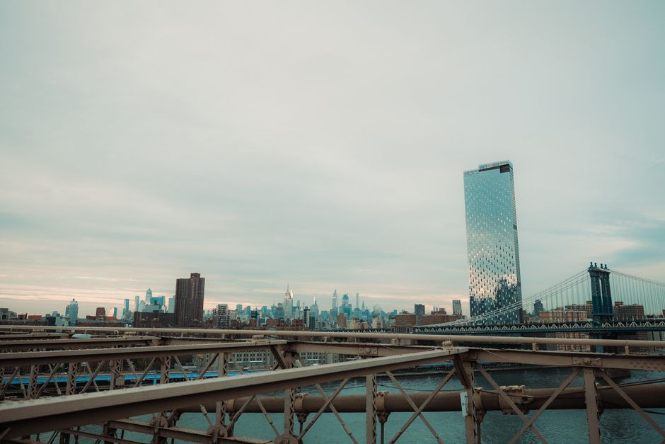 Stunning view of New York City skyline and Manhattan Bridge under a cloudy sky.