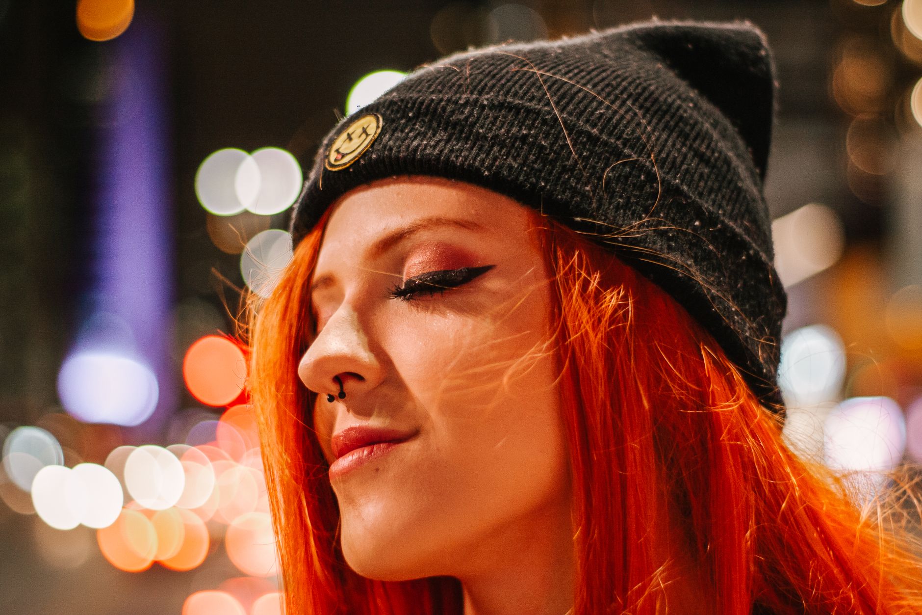 Portrait of a stylish woman wearing a beanie, illuminated by urban bokeh at night.