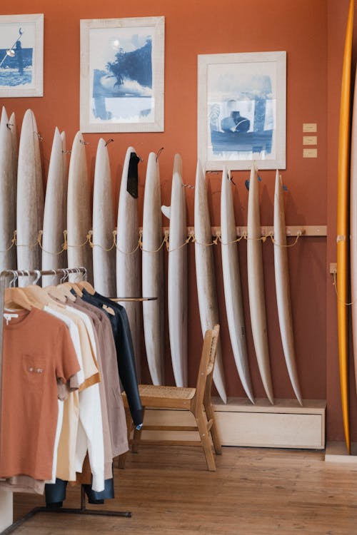 A room with surfboards on racks and clothes hanging on the wall