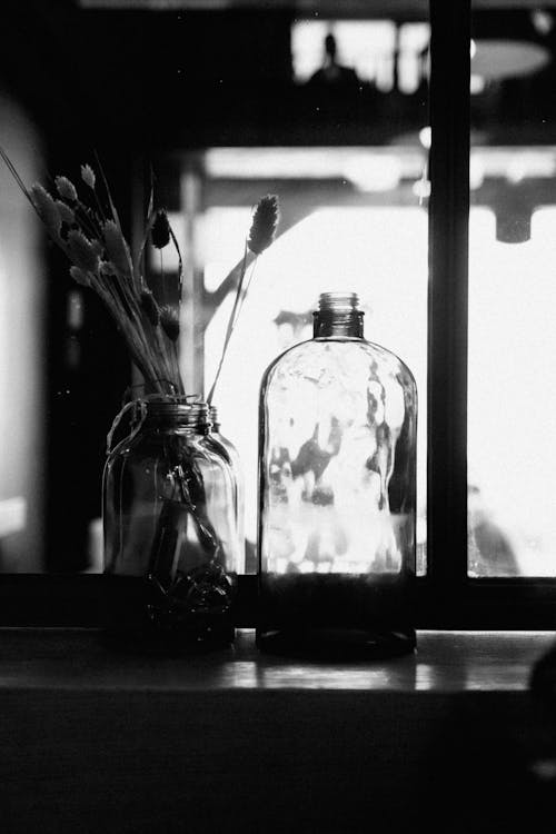 Black and white photograph of two glass bottles with flowers