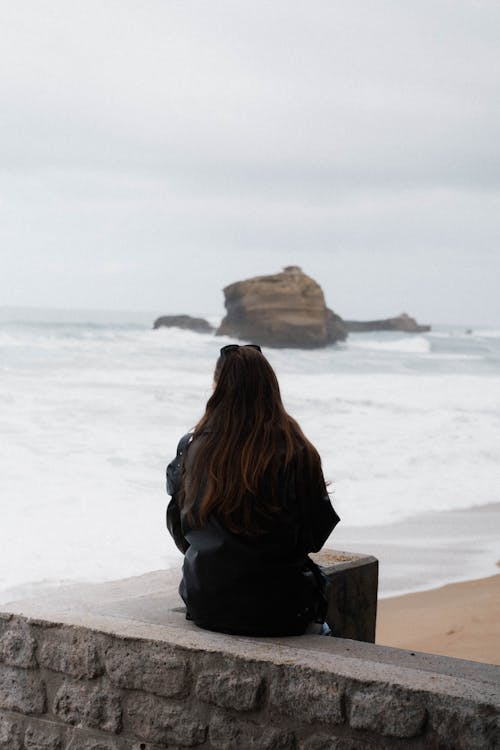 A woman sitting on a ledge looking out to the ocean