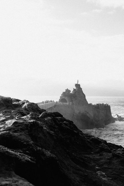 Captivating black and white photo of Rocher de la Vierge in Biarritz, featuring rocky coast and ocean mist.