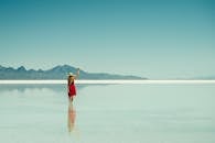 一位身着红色连衣裙的女人，站在宁静的盐滩上，背景是连绵的山脉，她正享受着孤独与反思