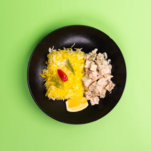 A black plate with chicken and rice on top of a green background