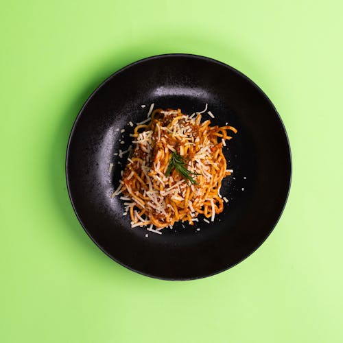 A black plate with spaghetti on it on a green background