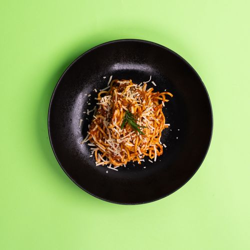 Free Top view of spaghetti with tomato sauce and cheese on a black plate against a green background. Stock Photo
