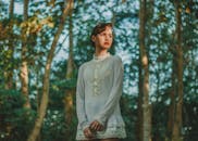 阳光明媚的树木中，一位身穿白色反光复古连衣裙的女人站在那里