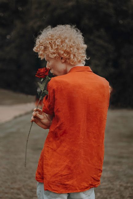 Back view of a person with curly hair holding a rose, set in a natural outdoor environment.
