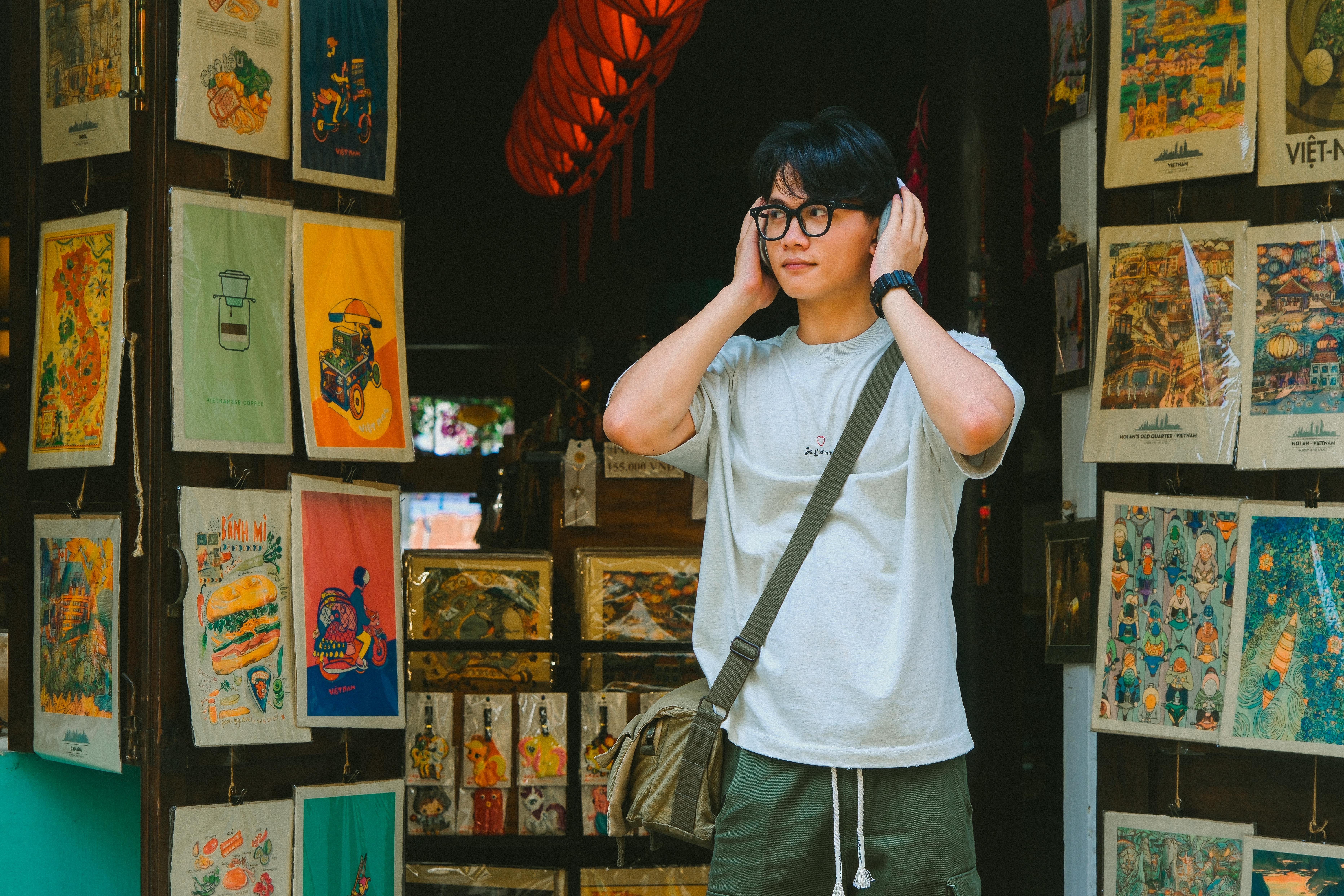 Man with glasses stands in colorful Vietnamese souvenir store, surrounded by artwork and decor.