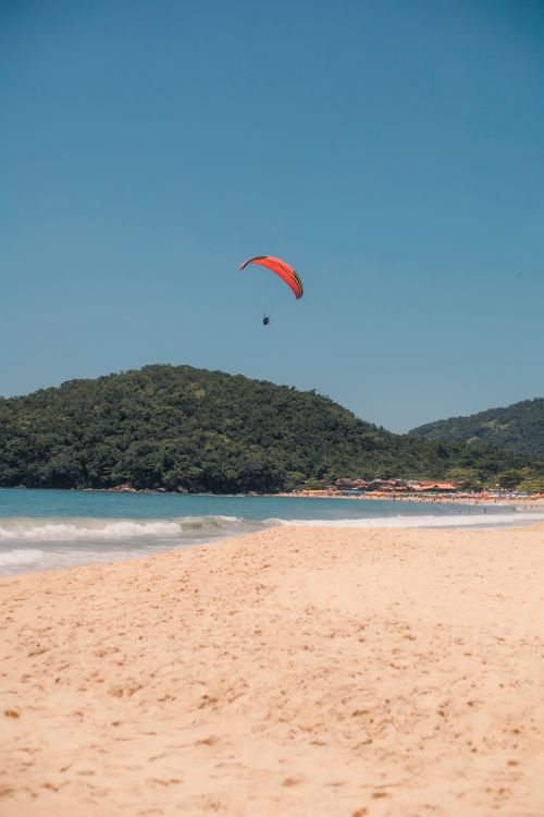 Free Experience the thrill of paragliding above the scenic beach of Paraty, Brazil on a clear summer day. Stock Photo