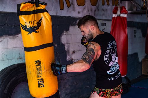 Free Tattooed man practicing boxing techniques indoors with a punching bag. Stock Photo