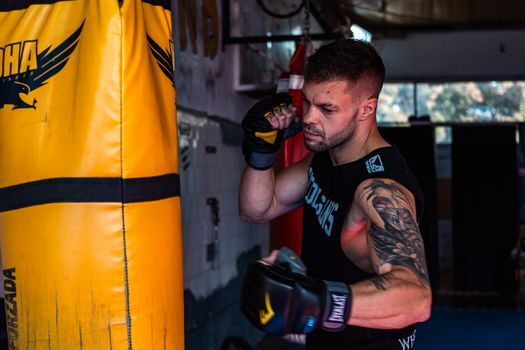 A man intensely trains in the gym, punching a heavy bag, showcasing strength and fitness.