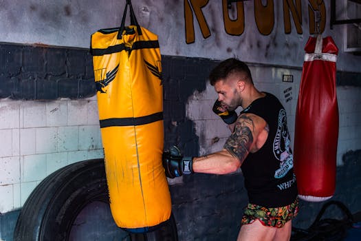 Young male boxer training with a yellow punching bag indoors, showcasing fitness and strength.