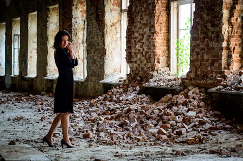 Woman in Black Dress Standing in Front of Pile of Bricks