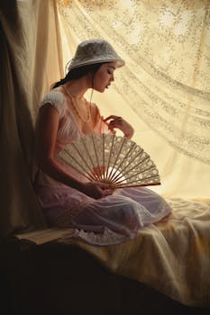 一位优雅的女子身着复古连衣裙，手持扇子，坐在柔和的灯光下