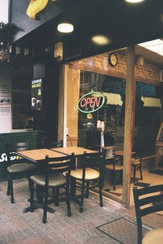 A charming café exterior featuring an 'Open' sign and outdoor seating for warm gatherings.