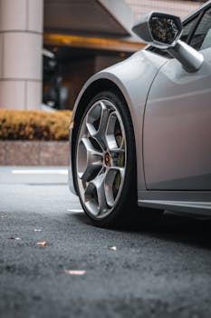 Close-up of a luxury silver Lamborghini sports car on city streets with focus on wheel and side mirror.