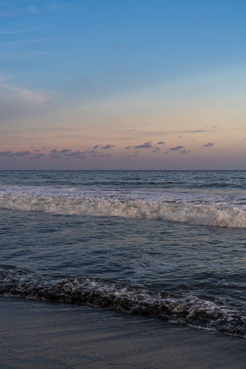 Free A serene view of ocean waves gently rolling onto a beach at dawn with a pastel sky. Stock Photo