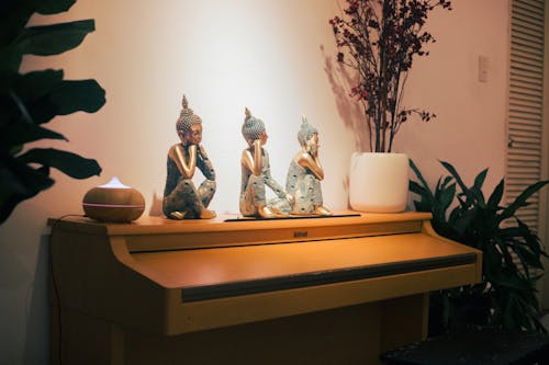 Three Buddha Sitting Figurines Near Oil Diffuser on Top of Piano