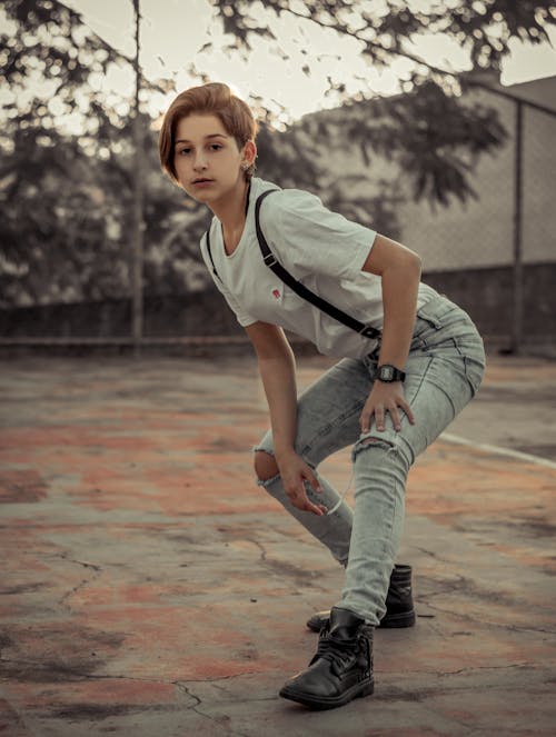 Photo of Woman in Grey Ripped Jeans, White T-shirt , and Suspenders Posing 