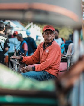 熙熙攘攘的城市人群中，一个穿红衬衫的成年男子坐在人力车上