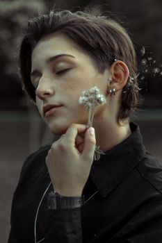 这幅肖像画描绘了一位闭着眼睛、手持蒲公英的年轻人，展现了穿孔和短发，画面宁静